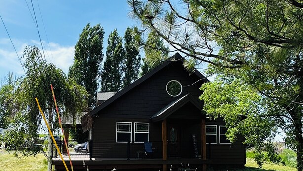 A wooden cabin with a porch, surrounded by tall grass and trees.