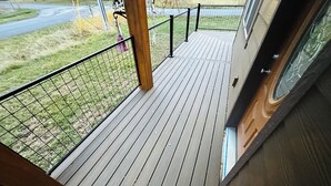A wooden deck with a metal railing, a view of the road, and a grassy area.