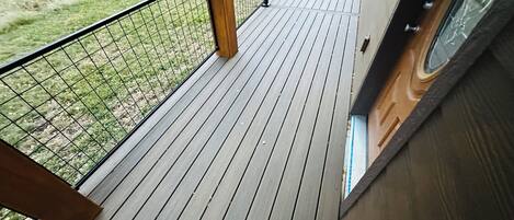 A wooden deck with a metal railing, a view of the road, and a grassy area.