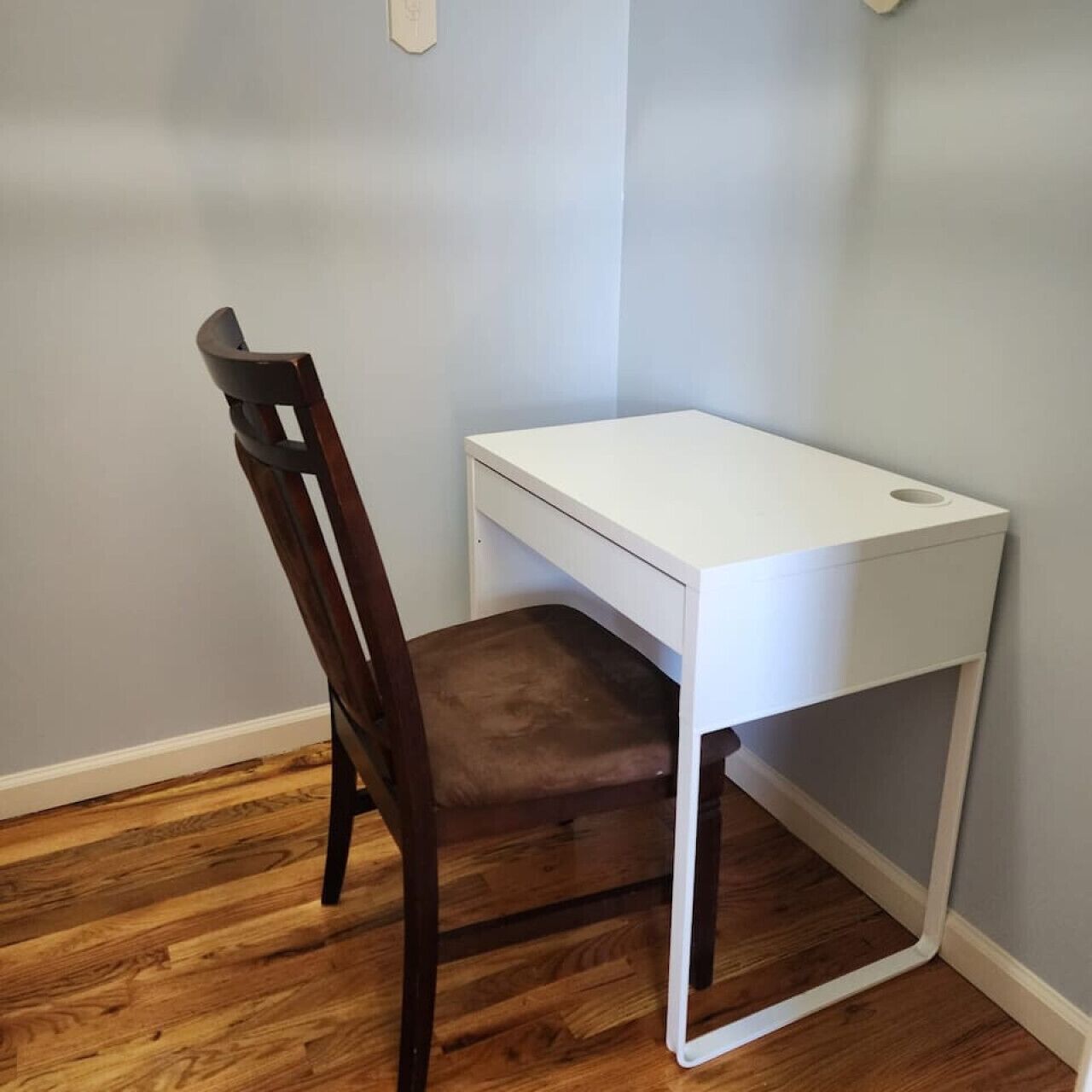 A corner desk with a chair, a white wall, and wooden flooring.