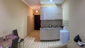 A compact kitchen with a refrigerator, sink, and cabinets. There is a dining table with chairs and a flower vase. - horizont building (Batumi)