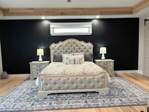 A bedroom with a tufted headboard bed, two bedside tables with lamps, a dark wall, a window, and a patterned rug. - Spacious 5-bedroom house on Monkey Island, Afton with WiFi, AC & slip in dock (Afton)