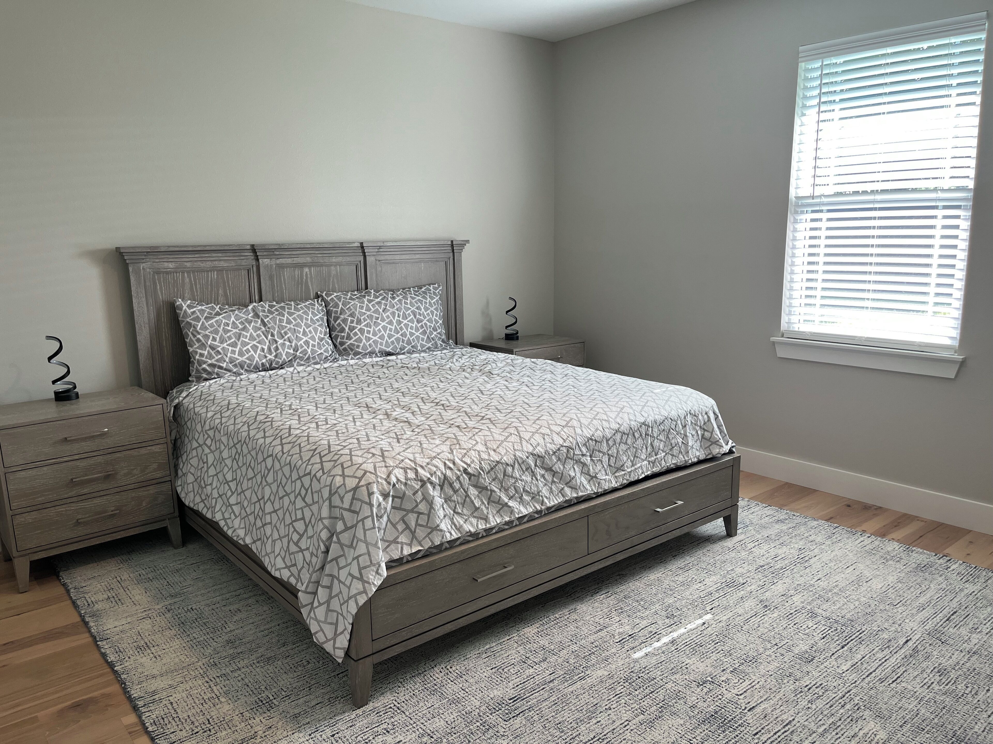 A bedroom with a bed, nightstands, a dresser, and a window with blinds.