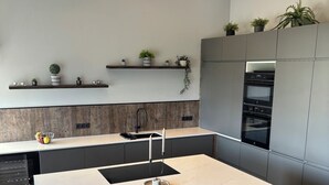 Una cocina moderna con una isla central, taburetes negros tipo barra, horno empotrado y salpicadero de madera.