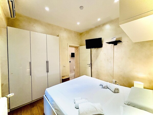 Un dormitorio con una cama grande, un televisor en la pared y un armario.