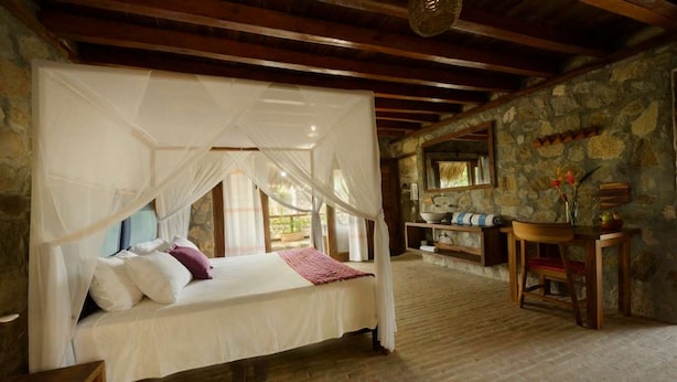 Een slaapkamer met een hemelbed, een stenen muur en een rustiek houten plafond.
