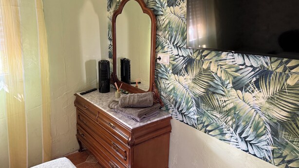Une salle de bain avec un meuble-lavabo en bois, un miroir et un mur orné d’un motif de feuilles tropicales.