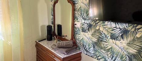 A bathroom with a wooden vanity, a mirror, and a wall with a tropical leaf pattern.