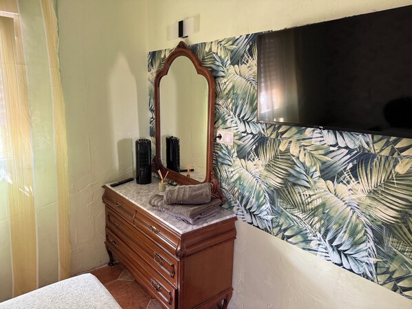A bathroom with a wooden vanity, a mirror, and a wall with a tropical leaf pattern.