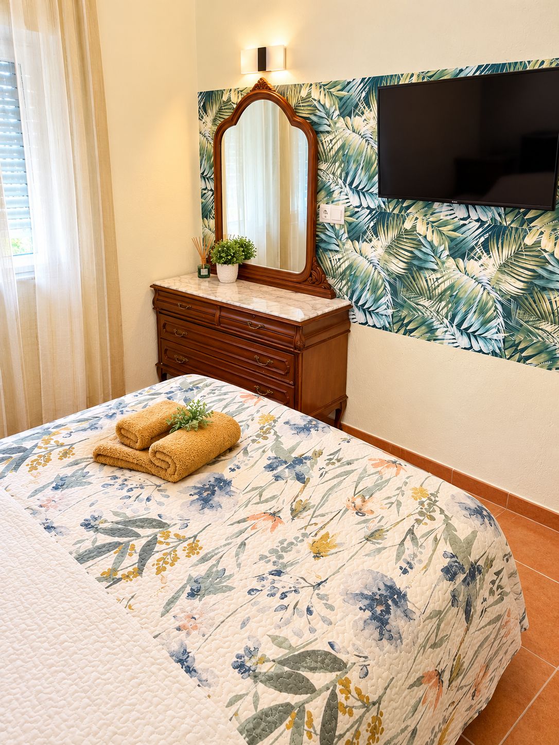 A hotel room with a bed, a dresser, a mirror, a television, and a window with curtains.