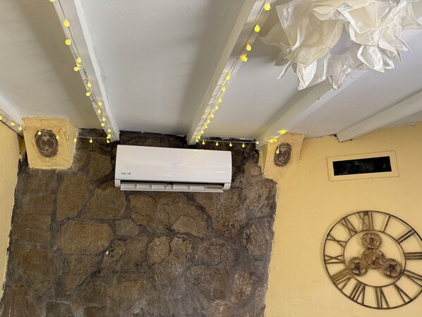 Un equipo de aire acondicionado montado en una pared de piedra, con un reloj decorativo y luces colgantes encima.