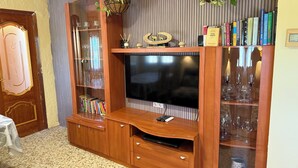 Un meuble de rangement en bois abritant un téléviseur à écran plat, des étagères avec des portes en verre et des plantes suspendues.