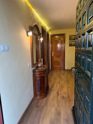 Un pasillo con suelo de madera, una puerta de madera, un espejo con iluminación y un armario empotrado.
