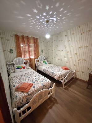 Un dormitorio con dos camas individuales, proyector en el techo, papel tapiz a rayas y suelo de madera.