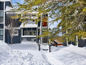 A snow-covered outdoor area with a building featuring a balcony and a red sign. - Lakeview Condo (Big Bear Lake)