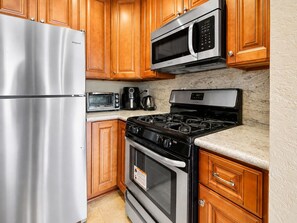 A kitchen with a stainless steel refrigerator, a microwave, a coffee maker, a stove, and wooden cabinets. - Lakeview Condo (Big Bear Lake)