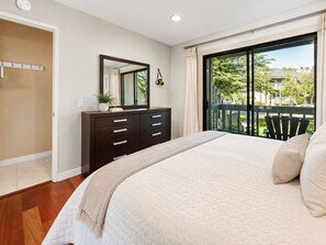 Un dormitorio con una cama grande, un aparador, un espejo y vistas a un balcón con mobiliario exterior.