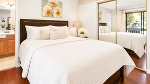 Une chambre d’hôtel avec un grand lit, une table de chevet avec une lampe, un miroir et un tableau représentant des fleurs accroché au mur.