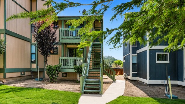 Un bâtiment doté d’un escalier vert menant à un balcon, entouré d’une pelouse bien entretenue et d’arbres.