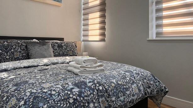 A bedroom with a bed, a painting of a beach, and blinds on the windows.