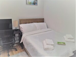 Habitación de hotel con cama, escritorio con computadora y ventana con vista a follaje.