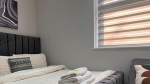 A neatly made bed with a quilted white duvet, a grey upholstered headboard, and a grey upholstered armchair with a cushion.