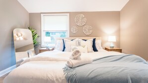 Un dormitorio con una cama grande, dos mesitas de noche, un tocador, un espejo y decoración en la pared.