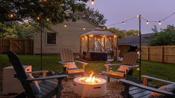Un espacio al aire libre con sillas Adirondack, una chimenea y luces colgantes.