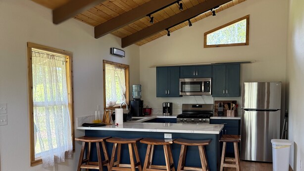 Une cuisine avec des meubles de couleur bleu foncé, un réfrigérateur en acier inoxydable et un îlot central en bois avec des tabourets.