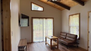 Un vaste salon doté de planchers en bois, d’un ventilateur de plafond, d’un canapé, d’une table basse et d’une porte-fenêtre coulissante donnant sur un espace extérieur.