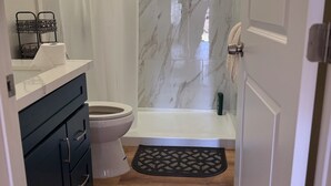 Une salle de bain comprenant des toilettes, une baignoire, un rideau de douche, un porte-serviettes et un miroir.