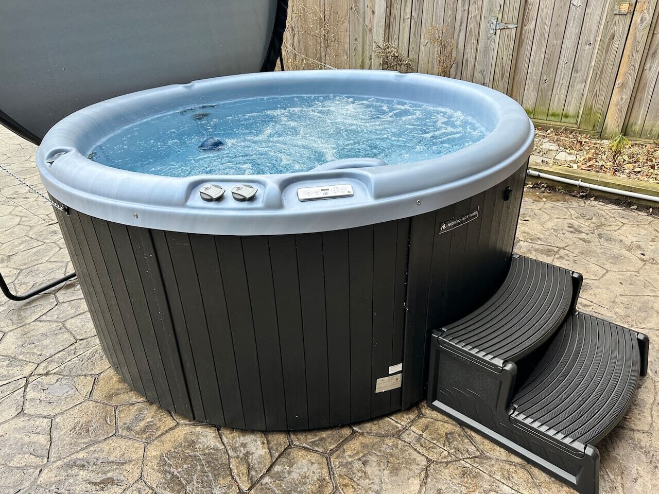 A hot tub with a control panel and steps, placed on a stone patio.