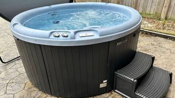 A hot tub with a control panel and steps, placed on a stone patio.