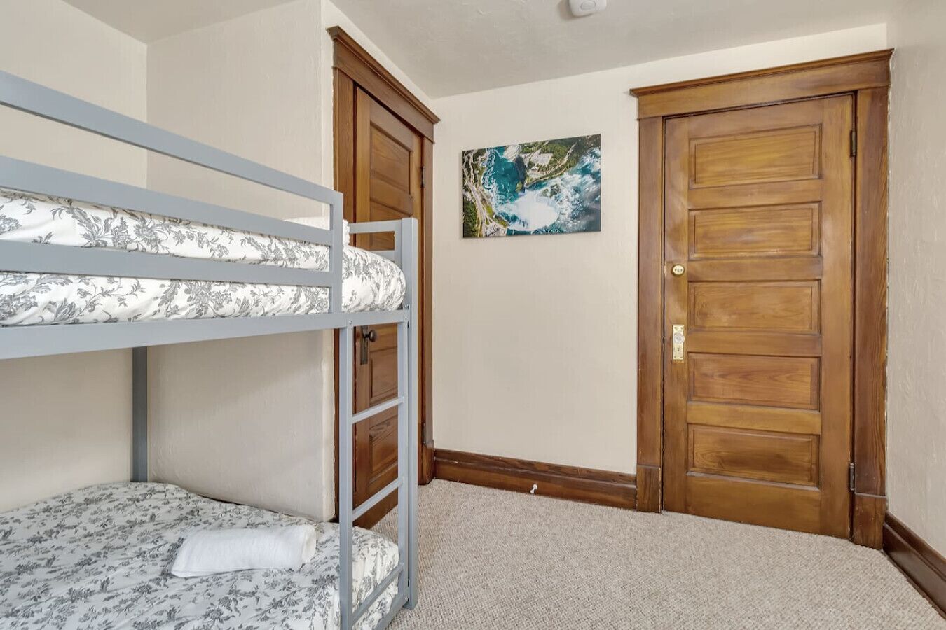 A bedroom with a bunk bed, two wooden doors, and a painting on the wall.