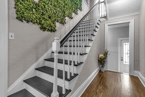 Eine Treppe mit weißen Balustern und dunklen Stufen, die zu einem Raum mit Holzboden und einer Tür mit dekorativem Glas führt.