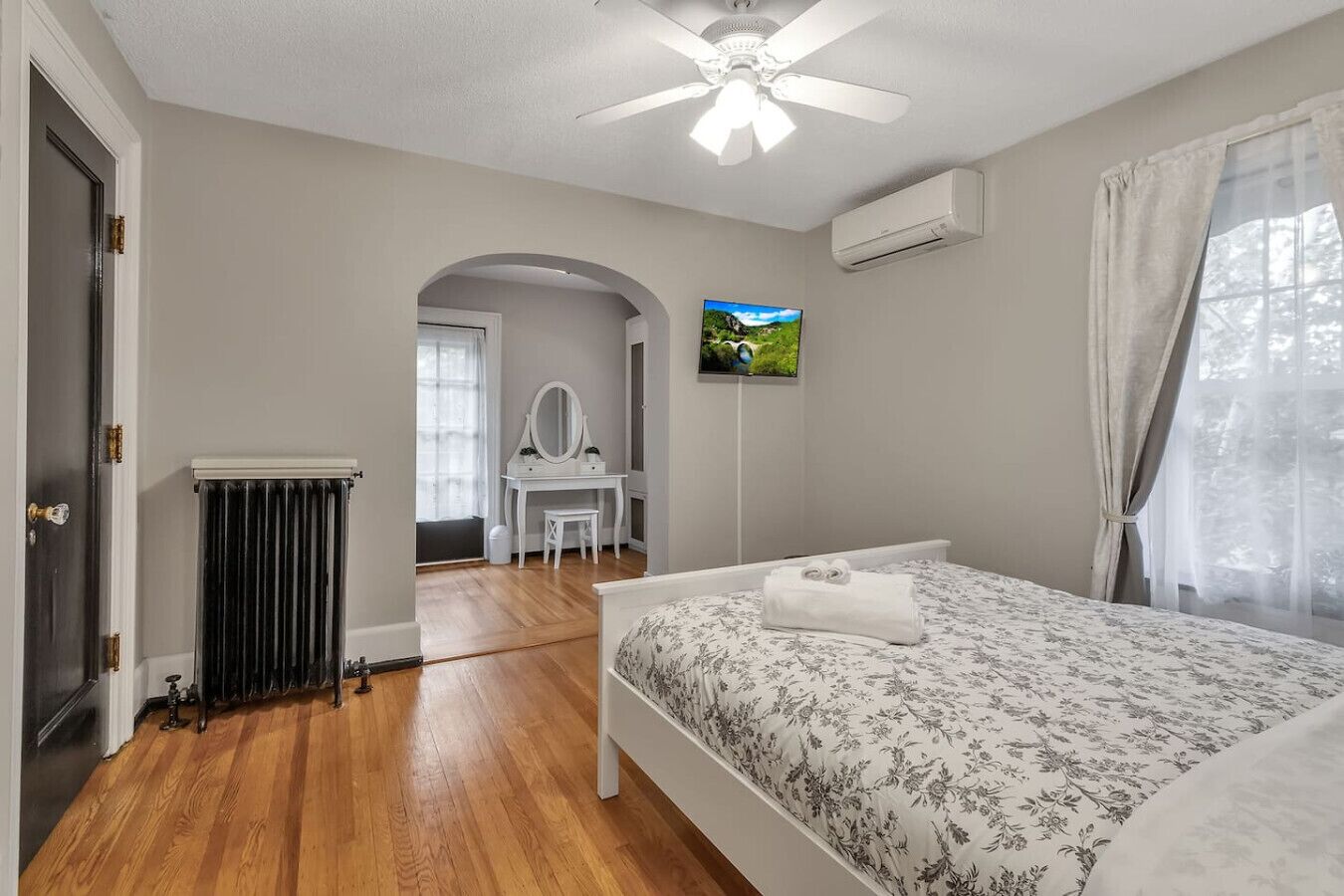 A bedroom with a bed, a vanity, a television, and a radiator.