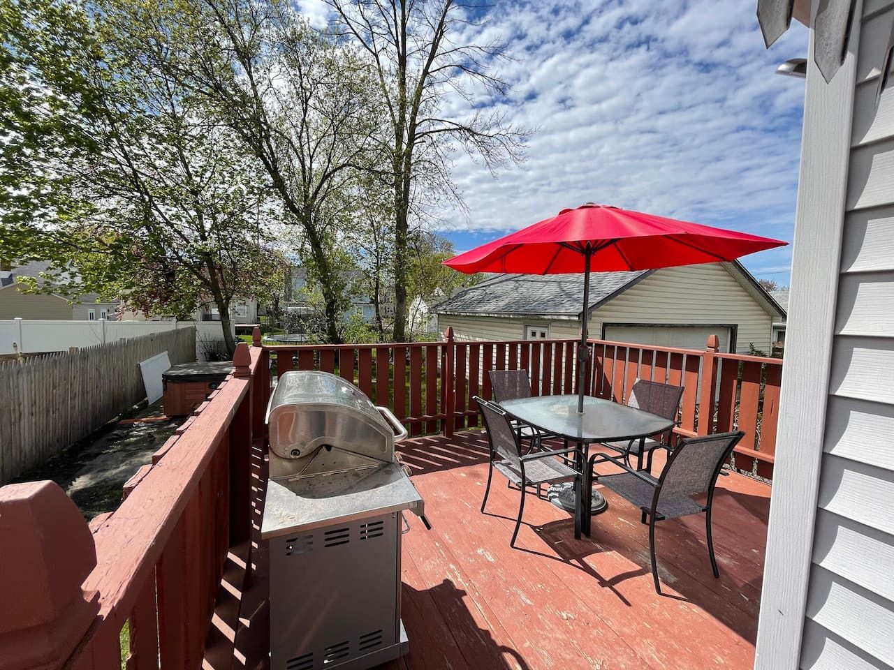 Une terrasse avec un barbecue, une table et un parasol rouge.