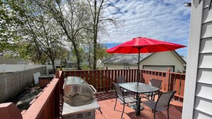 Un patio con una parrilla, una mesa y un paraguas rojo.