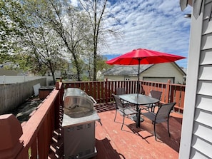 A patio with a grill, a table, and a red umbrella.