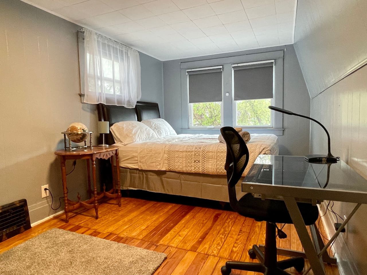 Une chambre à coucher avec un lit, un bureau, une chaise, une lampe et une fenêtre.