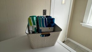 Una cesta blanca de ropa con prendas dobladas sobre un electrodoméstico blanco, probablemente una lavadora, en una habitación con paredes color beige y una puerta blanca.