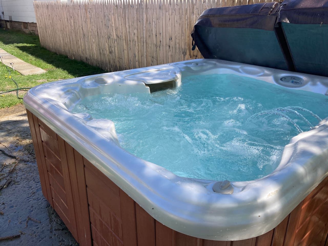 A hot tub with a wooden exterior and a metallic interior, surrounded by a wooden fence and a grassy yard.