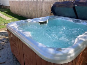 A hot tub with a wooden exterior and a metallic interior, surrounded by a wooden fence and a grassy yard.