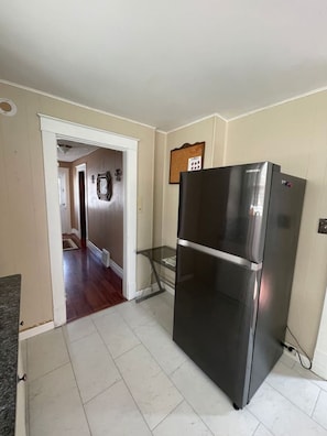 Cocina con refrigerador de acero inoxidable, repisa de vidrio y puerta que da a otra habitación.