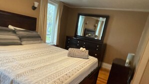 Un dormitorio con una cama grande, un aparador, un espejo y una mesita de noche pequeña.