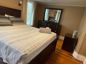 A bedroom with a large bed, a dresser, a mirror, and a small nightstand.