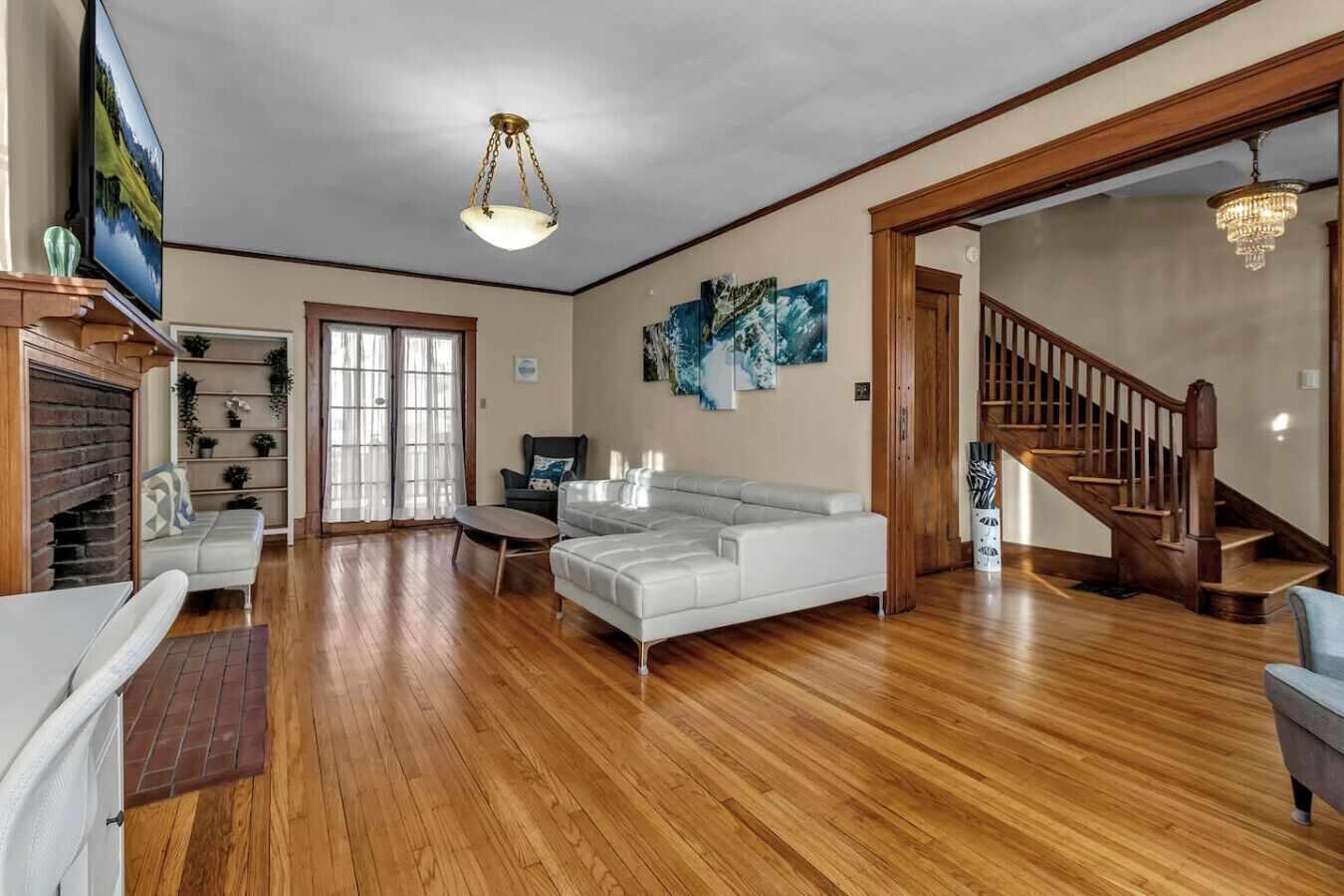 A spacious living room with hardwood flooring, a white sectional sofa, a television, and a staircase leading to another level.