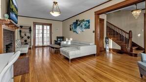 A spacious living room with hardwood flooring, a white sectional sofa, a television, and a staircase leading to another level. - Spacious ♥ Niagara Falls♥A/C♥Parking♥Steam Shower (Niagara Falls)