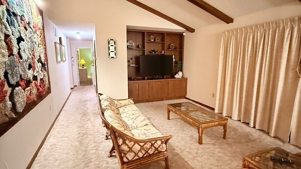 Una sala de estar con un sofá, dos sillones, una mesa de centro, un televisor y una pared decorada con una obra de arte colorida.
