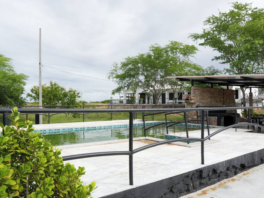Una piscina amb una estructura de pedra i baranes metàl·liques, envoltada de vegetació i un cel nuvolós.